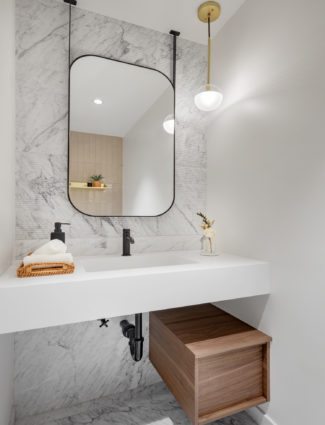 Ribbed white marble accent wall with black rectangular mirror suspended from ceiling and white bathroom vanity countertop