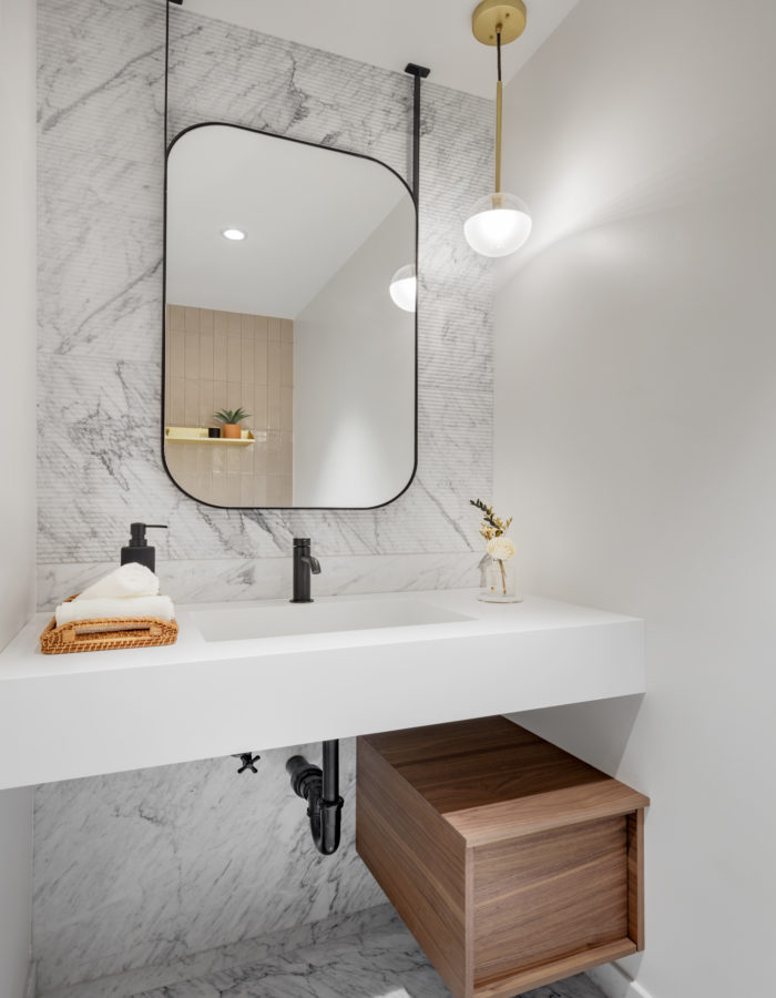 Ribbed white marble accent wall with black rectangular mirror suspended from ceiling and white bathroom vanity countertop