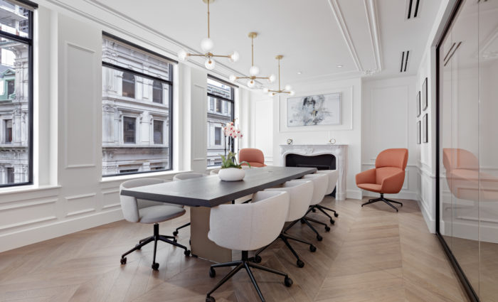 Angled view of Boston office conference room with beige chairs, dark wood table, marble fireplace and designer lighting.