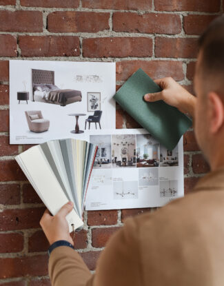 Designer holding up paint and fabric swatches to moodboard on brick wall