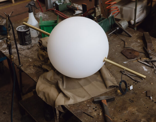White glass sphere light fixture with brass detail sitting on workshop table