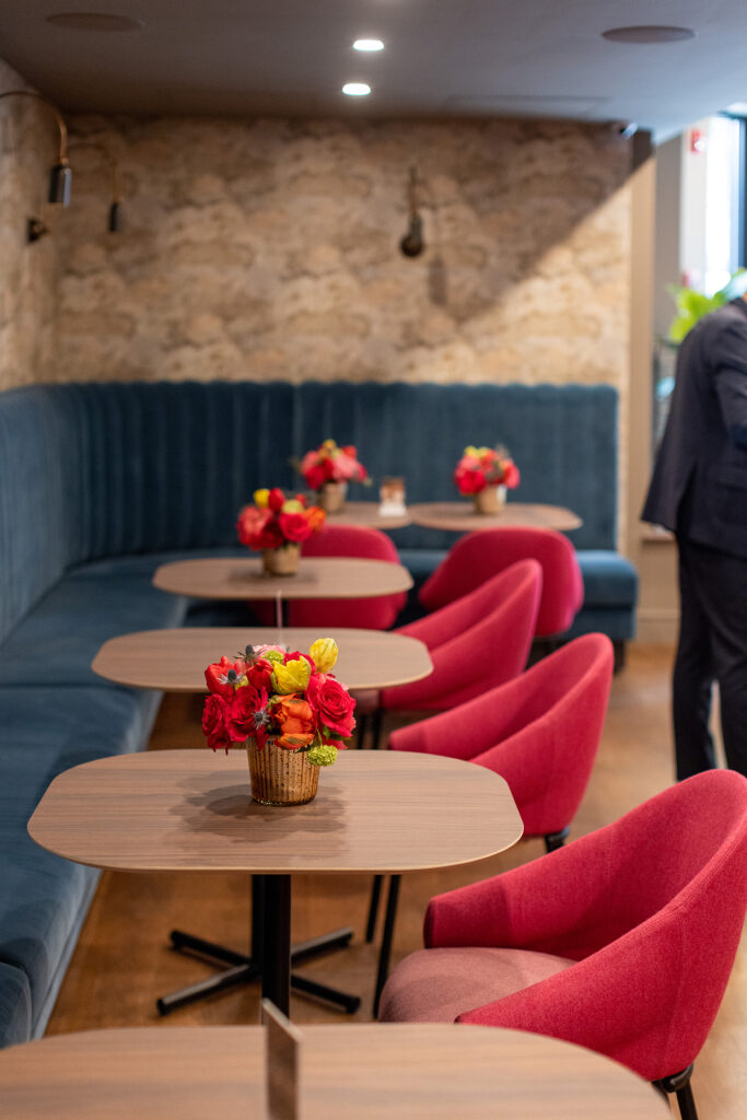 Custom furniture for Sabina Mezcaleria with fuchsia pink chairs, light blue velour tufted banquette and wood veneer table tops with floral arrangements 