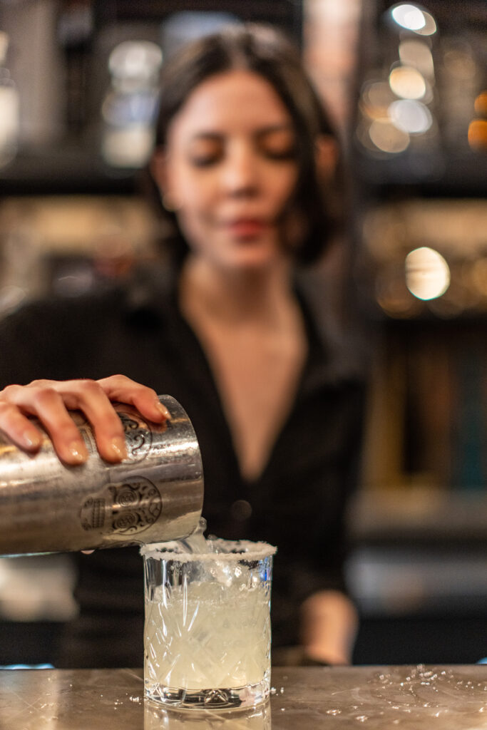 Bartender pouring signature margarita drink into a glass over custom bar